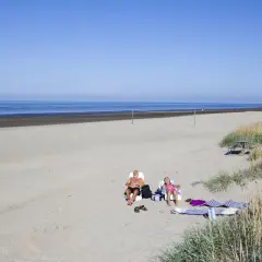 Två personer solar på stranden vid Björkäng camping. En man och en flicka njuter av solen.