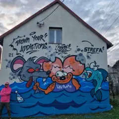 Kolorowy mural na domu jednorodzinnym przedstawia kreskówkowe zwierzęta w wodzie. Widać mysz, małpkę z napisem "LIFE GUARD" i rybę.