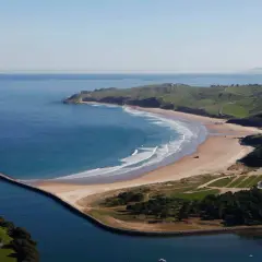 Impresionantes playas cerca de San Vicente de la Barquera, con olas rompiendo en la arena dorada y verdes colinas al fondo.