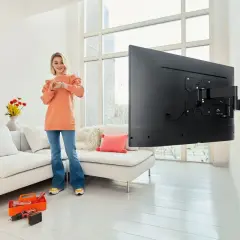 Kobieta sprawdza zegarek, zastanawiając się, na jakiej wysokości telewizor będzie idealnie zamontowany. Obok narzędzia do montażu.