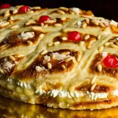 Deliciosa coca de San Juan rellena de crema, decorada con piñones, cerezas rojas y azúcar.