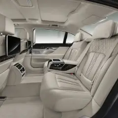 Luksusowe wnętrze BMW serii 7 z jasnymi, pikowanymi fotelami i ekranami multimedialnymi dla pasażerów z tyłu.