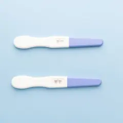 Dwa testy ciążowe na jasnoniebieskim tle. Jeden pokazuje jeden pasek, drugi dwa. Kiedy zrobić test ciążowy?