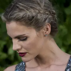 Mujer con elegante peinado con trenzas, maquillaje dramático y vestido brillante.