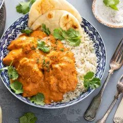 Aksamitny kurczak po indyjsku w pomarańczowym sosie, podany z ryżem basmati i chlebkiem naan. Udekorowany świeżą kolendrą.