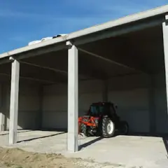 Capannone prefabbricato in cemento in zona agricola, ideale per chi vuole costruire in zona agricola senza essere imprenditore agricolo. Un trattore è parcheggiato all'interno.
