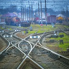 Skrzyżowanie torów kolejowych z widocznym wskaźnikiem W20. W tle stoją wagony towarowe.