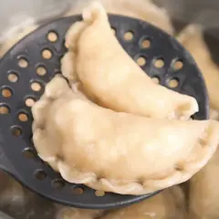 Gotowe pierogi z serem na łyżce cedzakowej, gotujące się w garnku. Idealne, by pokazać, jak zrobić pierogi z serem.