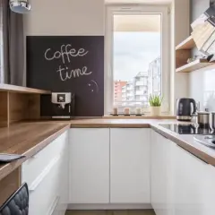 Biała kuchnia z drewnianym blatem, na którym stoi ekspres do kawy. Na tablicy napis "coffee time".