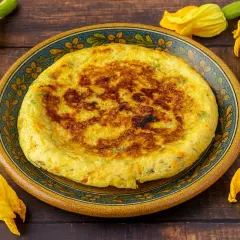 Frittata dorata con fiori di zucca, servita su un piatto decorato, circondata da fiori freschi.