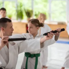 Nauczyciel pokazuje dziewczynce, jak używać nunchaku podczas treningu sztuk walki.