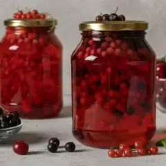 Dwa słoje domowego kompotu z czerwonej i czarnej porzeczki, ozdobione gałązkami owoców.