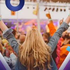 Radosna publiczność na koncercie, z rękami w górze. Zastanawiasz się, co zabrać na koncert? Ta dziewczyna ma świetny styl i opaskę na rękę.