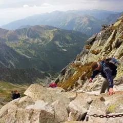 Wspinaczka na skalistym szlaku w Tatrach, widok na dolinę i pasma górskie. Świnicka przełęcz w oddali.