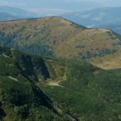 Widok na górzyste tereny, z wyraźnie zaznaczoną ścieżką na zboczu. W oddali widać kolejne pasma górskie. Przełęcz Kocierska w jesiennej odsłonie.