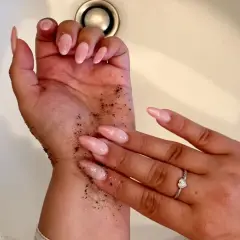 Exfoliante de café en la mano para quitar el autobronceador. Uñas largas y rosadas, anillo de corazón.