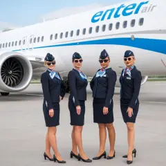 Cztery stewardessy Enter Air w granatowych mundurkach pozują przed samolotem. Czekają, by serwować pyszne jedzenie w przestworzach.