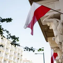 Biało-czerwona flaga powiewa na tle jasnego nieba, obok rzeźb atlantesów. Czy 2 maja jest wolny?