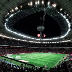 Widok na murawę i trybuny największego stadionu w Polsce. Rozświetlony dach i jupitery tworzą niesamowitą atmosferę.