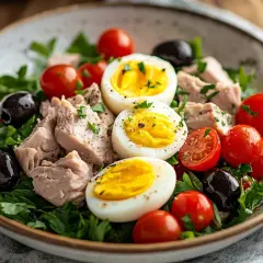 En härlig sallad nicoise med tonfisk, ägg, tomater och svarta oliver på en bädd av gröna blad.