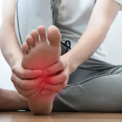Persona che si tiene il piede, con un'area rossa che indica dolore sotto pianta del piede al centro.
