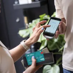 Kobieta wpisuje kod PIN na telefonie, trzymając kartę Visa. Czy płatność kartą w internecie jest bezpieczna? Tak, dzięki nowoczesnym zabezpieczeniom.