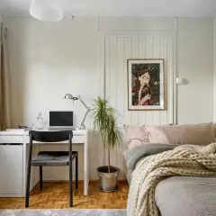 Gemütliches homeoffice im schlafzimmer mit Schreibtisch, Laptop und Bett. Ein Bild mit einer Frau und Pflanzen ziert die Wand.