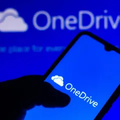 Dłoń trzyma smartfon z ikoną OneDrive. Szybki OneDrive download ułatwia dostęp do plików.