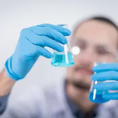 Naukowiec w niebieskich rękawiczkach bada płyn w kolbach. BHT może być kluczowym składnikiem w jego badaniach.