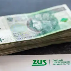 Stos banknotów 100 zł obok dokumentu ZUS. Może to symbolizować zarabianie na kontach bankowych lub oszczędzanie na przyszłość.