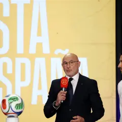 Mężczyzna w garniturze z mikrofonem i piłkarze Hiszpanii na tle napisu "LISTA DE ESPAÑA".