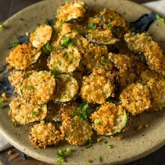 Fette croccanti di zucchine in friggitrice ad aria con pangrattato dorato, guarnite con prezzemolo fresco.