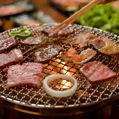Enjoying delicious yakiniku at home. Slices of raw beef sizzle on a grill over glowing coals, with green peppers and an onion ring adding color.