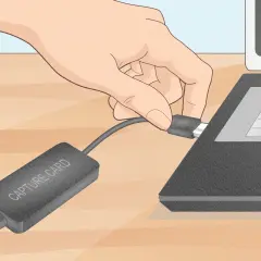 Dłoń podłącza kabel karty przechwytującej do laptopa.