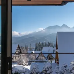Zimowy krajobraz z ośnieżonymi domkami i lasem, idealny na nocleg z pięknym widokiem na Tatry.