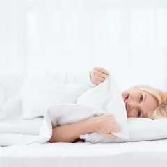 Uśmiechnięta kobieta w pościeli, czuje się komfortowo na materacu dla alergika.