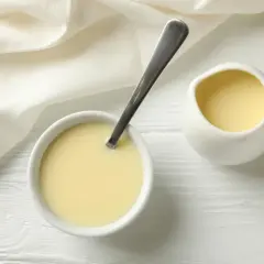 Crema amarilla en un cuenco con cuchara y jarrita, ideal para sustituir nata para cocinar por leche en recetas ligeras.
