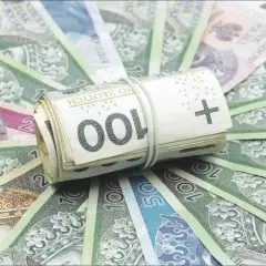 Zwijana rolka polskich banknotów 100 zł na tle innych banknotów.