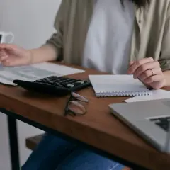 Osoba wypełnia deklarację podatek od nieruchomości, korzystając z kalkulatora i notatnika.