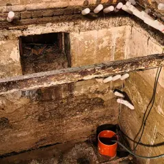 Feuchter Keller mit aufstauendem Sickerwasser, Rohren und einem Eimer zur Entwässerung.