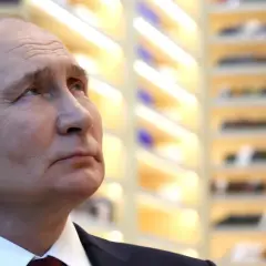 Nahaufnahme von Wladimir Putin, der nachdenklich in die Ferne blickt. Die Hintergrundbeleuchtung deutet auf eine Veranstaltung hin, vielleicht im Zusammenhang mit den Russland Wahlen.