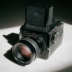 A classic Mamiya 645 medium format camera sits on a white surface, bathed in dramatic light and shadow.