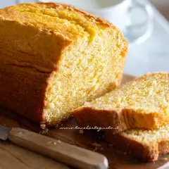 Plumcake senza yogurt dorato e soffice, tagliato a fette su un tagliere di legno con un coltello.