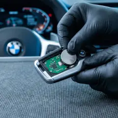 Rękawiczki ochronne ułatwiają wymianę baterii w kluczyku BMW. Widać deskę rozdzielczą i kierownicę.
