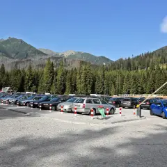 Parking pod Morskim Okiem, pełen samochodów, z górami i lasem w tle.