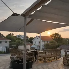 Sol segel skyddar en mysig uteplats med rottingmöbler. Solnedgången färgar himlen orange över villakvarteret.
