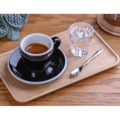 Czarna filiżanka espresso na drewnianej tacy, obok szklanka wody i łyżeczka. Idealnie pokazuje, jak podawać espresso.
