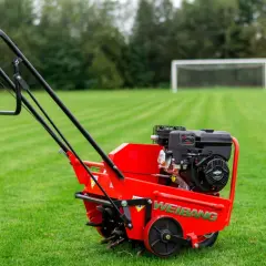 Czerwony aerator Weidemann na trawniku. Urządzenie to służy do napowietrzania gleby, poprawiając jej strukturę i zdrowie trawy.