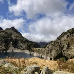 Paisaje montañoso con un embalse azul, ideal para rutas en Sallent de Gállego. Nubes y vegetación agreste completan la escena.