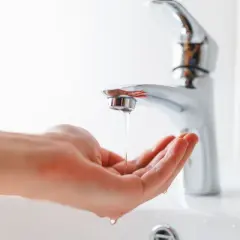 Main tenant, comment réduire la pression d'eau sur un robinet. Une main attrape un mince filet d'eau sortant d'un robinet moderne.